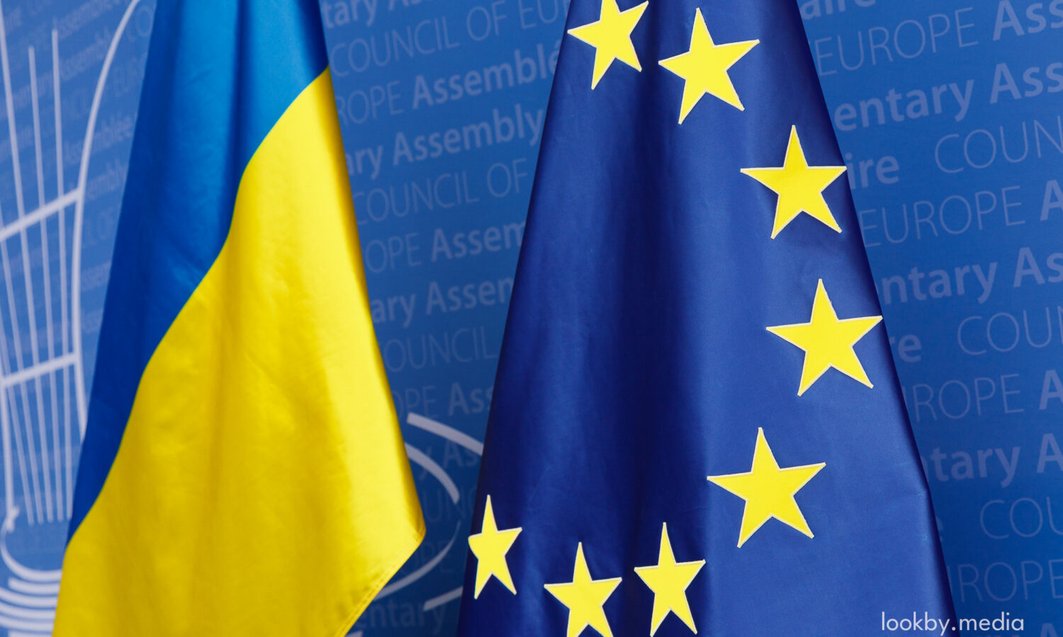Flags of Ukraine and Europe in front of PACE branding at the Palais de l’Europe.